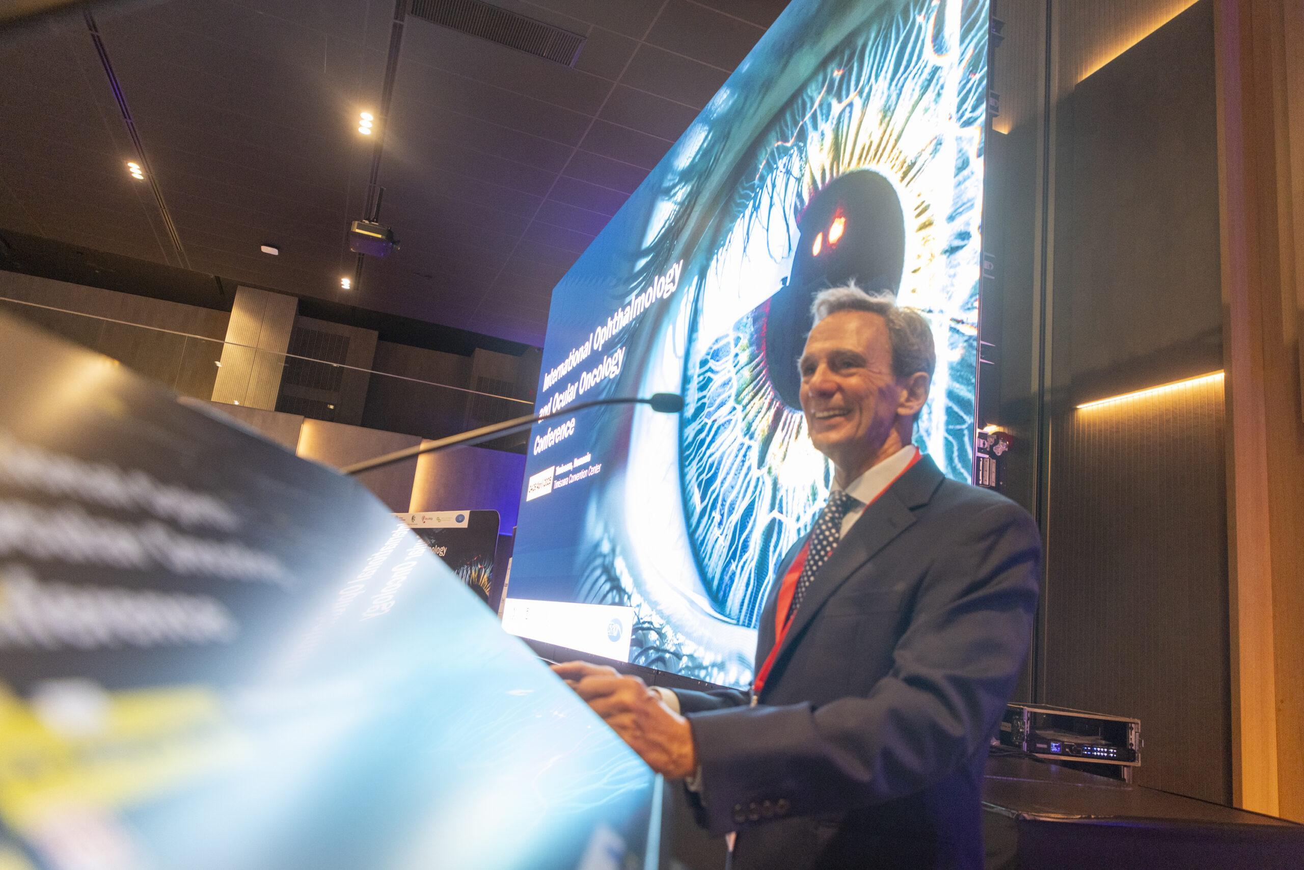 Man smiling at a podium with a screen behind him