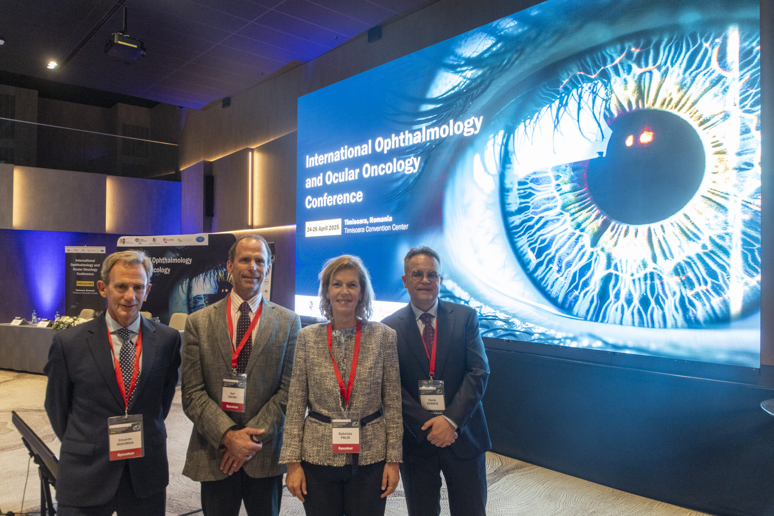 Four professionals wearing badges in front of a screen at a conference