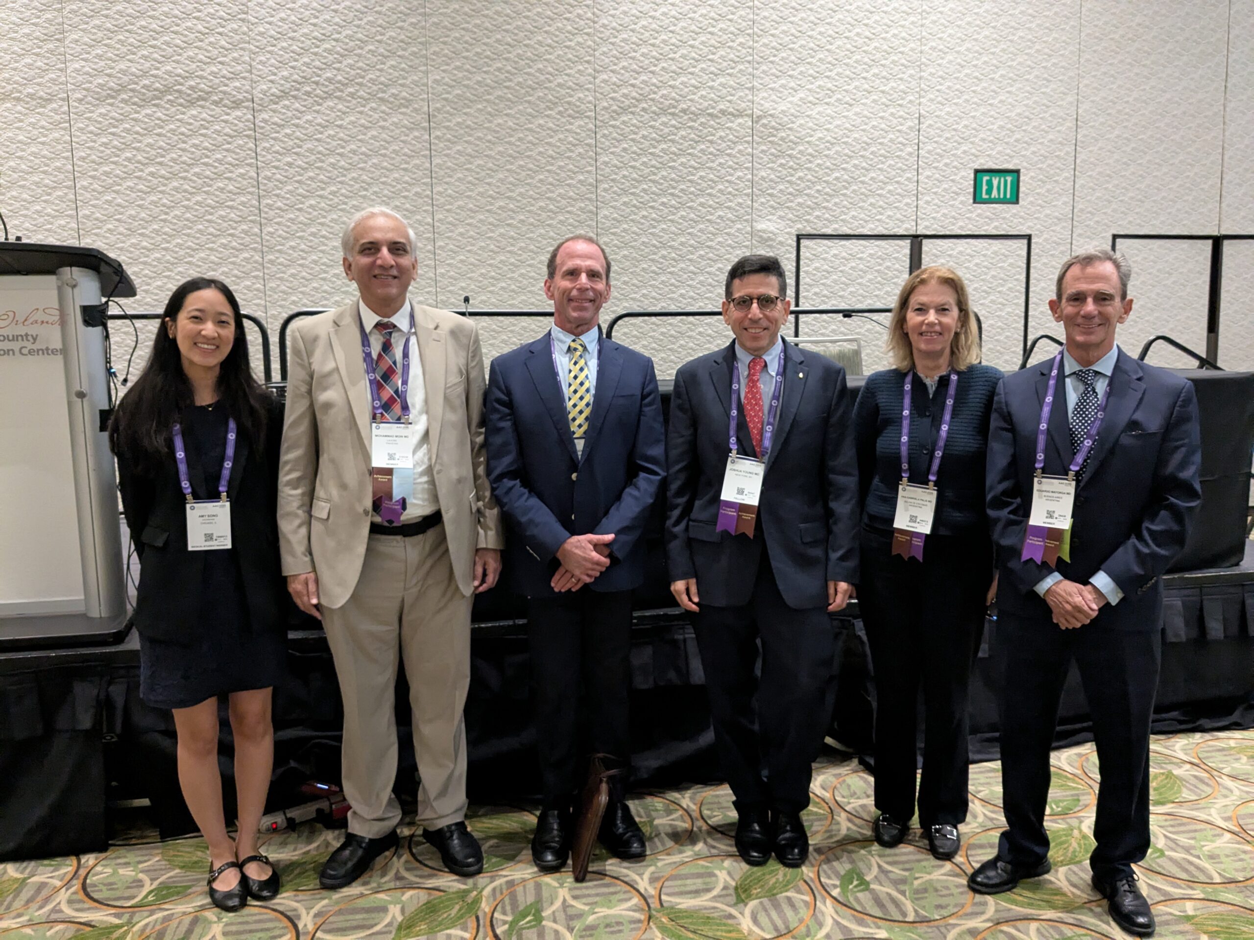 Five presenters posing in front of a stage in a conference room.