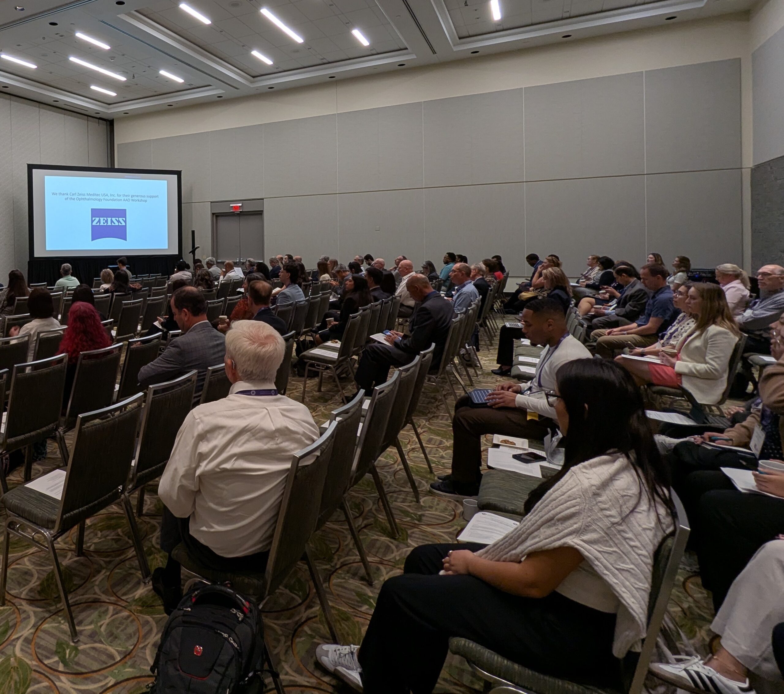 Five presenters posing in front of a stage in a conference room.