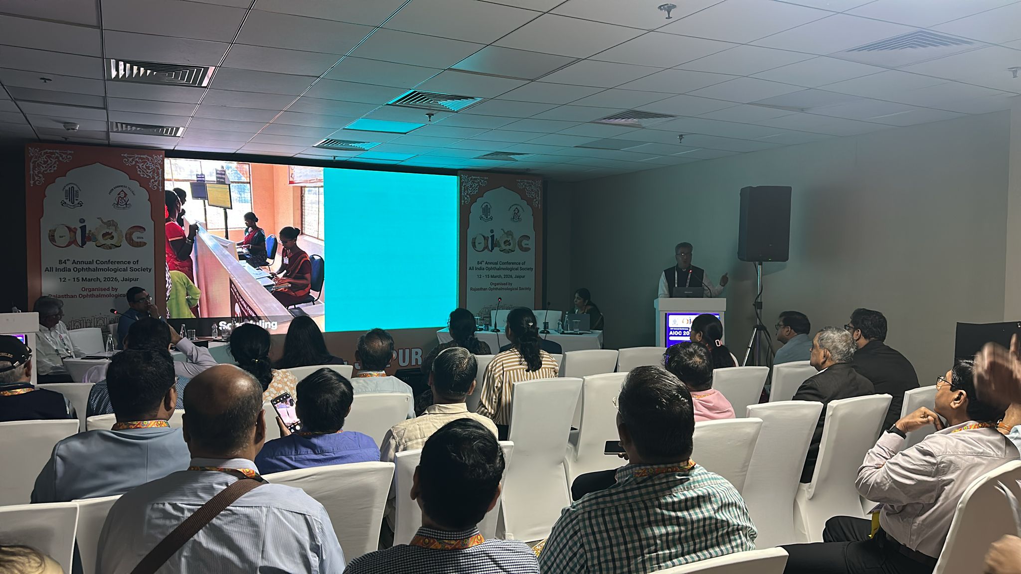 A professional man and woman in front of a screen for AMEE 2025
