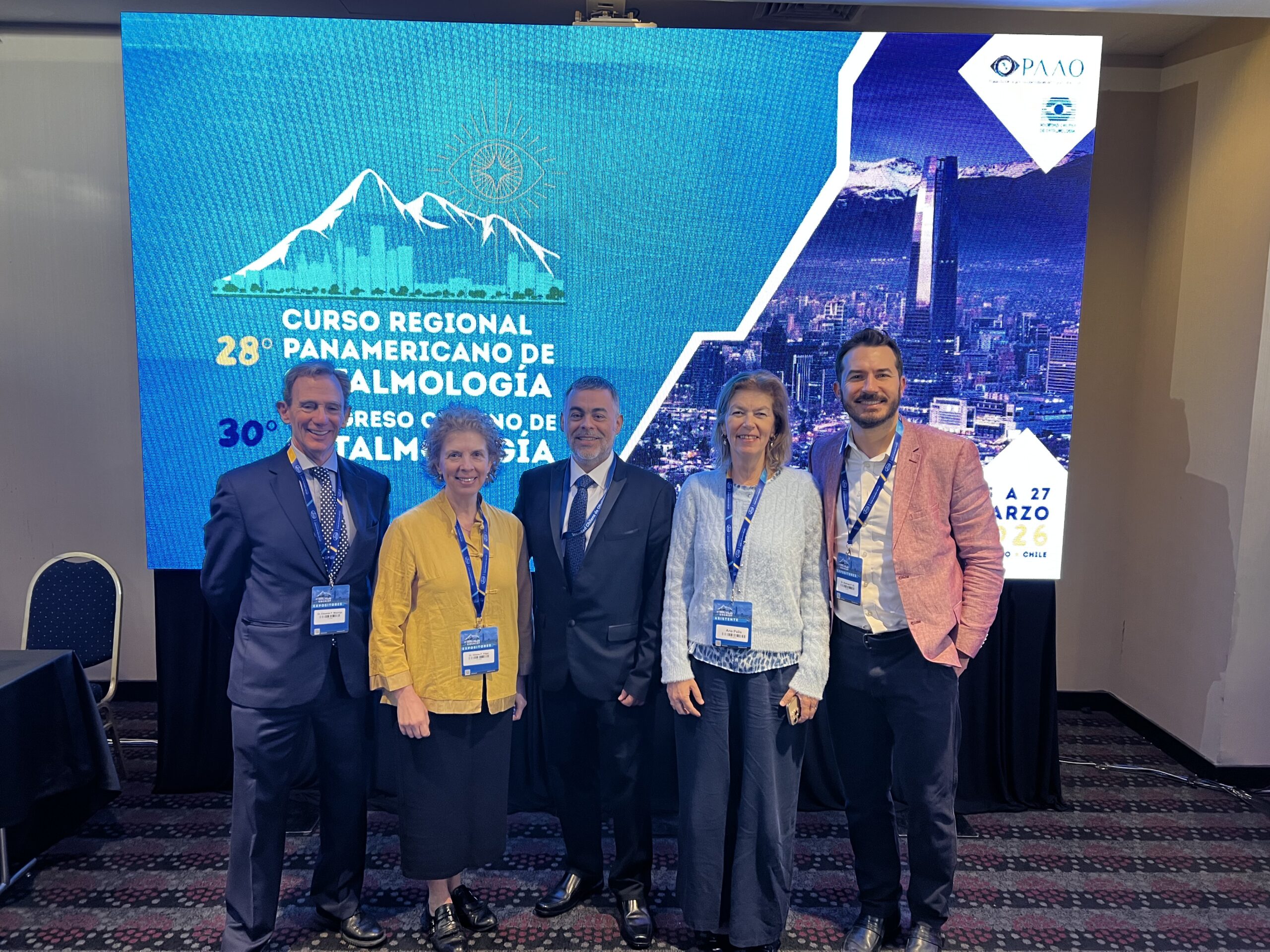 Four professionals wearing badges in front of a screen at a conference