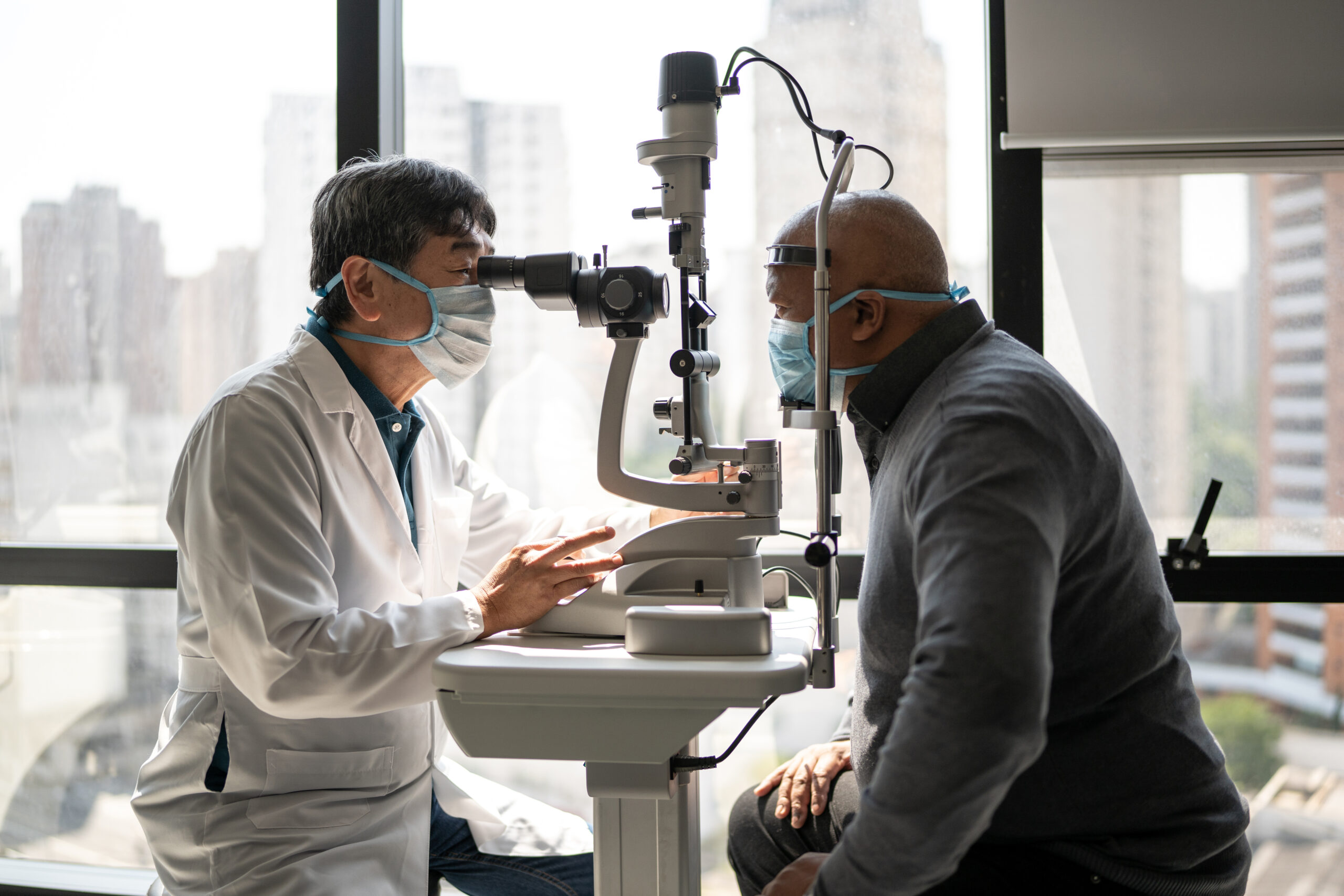 Optometrist examining patient's eyes - wearing face mask